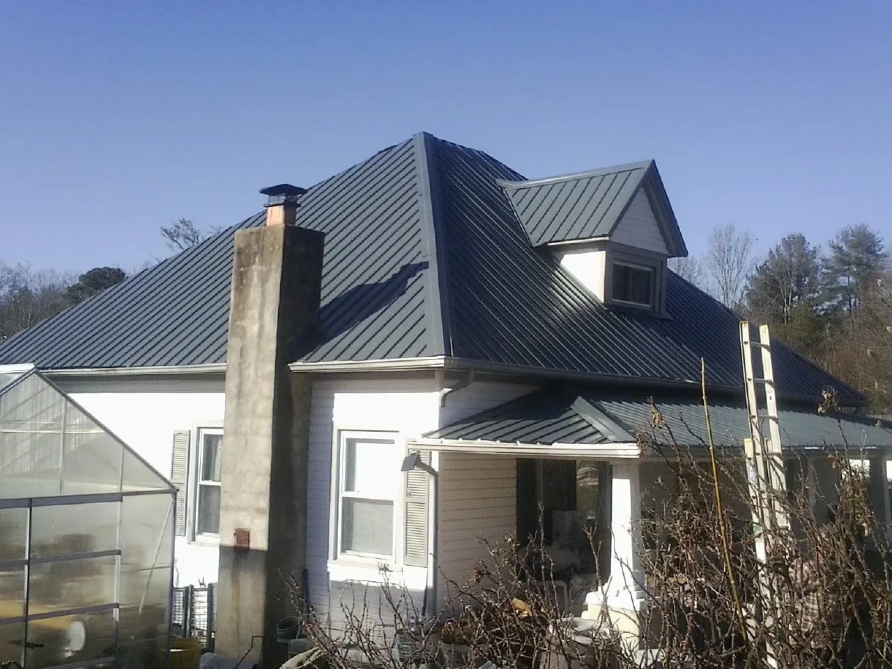 Dark blue standing seam metal roof on a white farmhouse with dormer — Slate & Tile Roof Repair by Roofing Brothers in North Sandwich