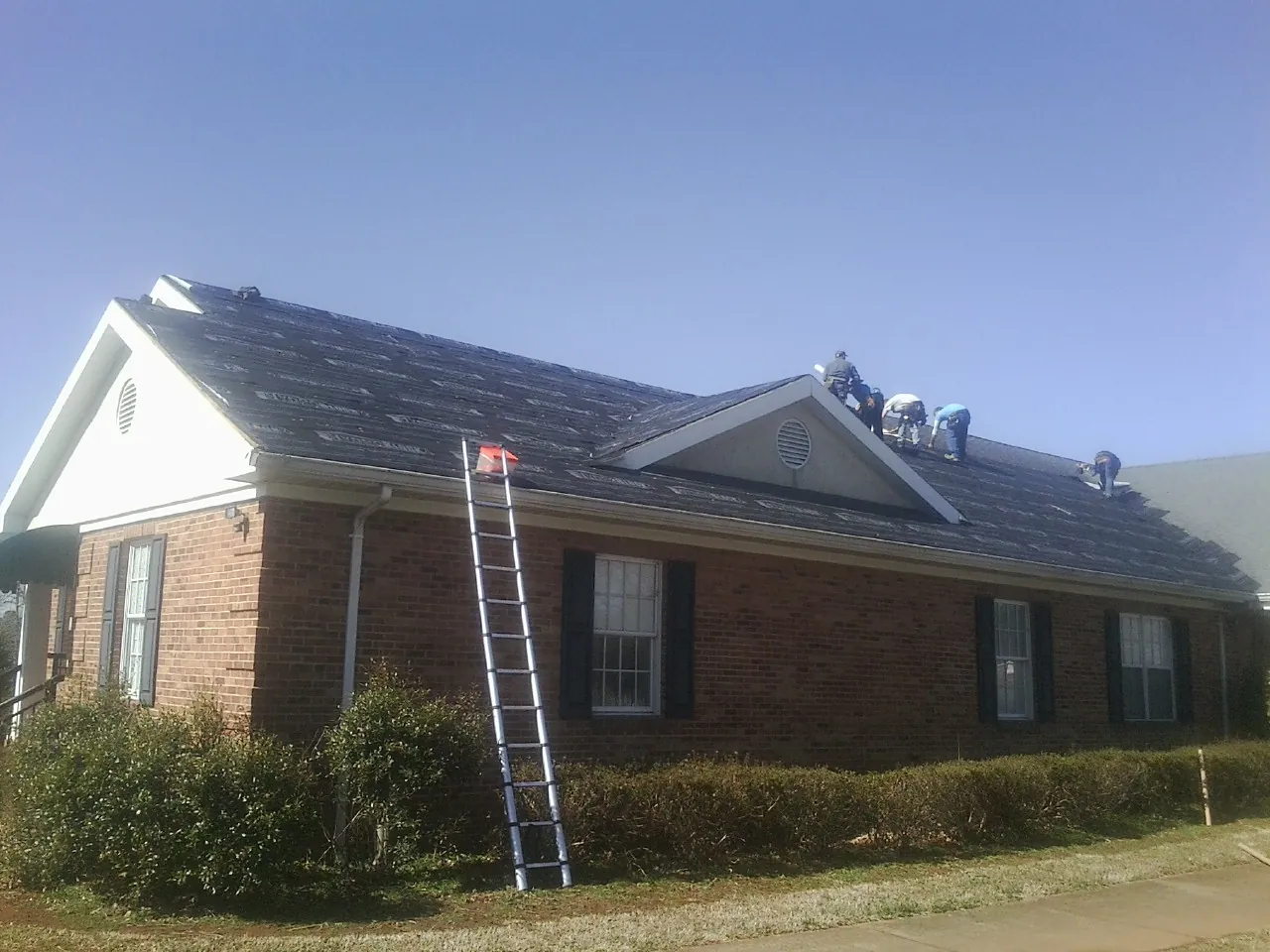 Crew tearing shingles off a brick ranch roof with a ladder set — Emergency Roof Repair work by our crew in North Sandwich