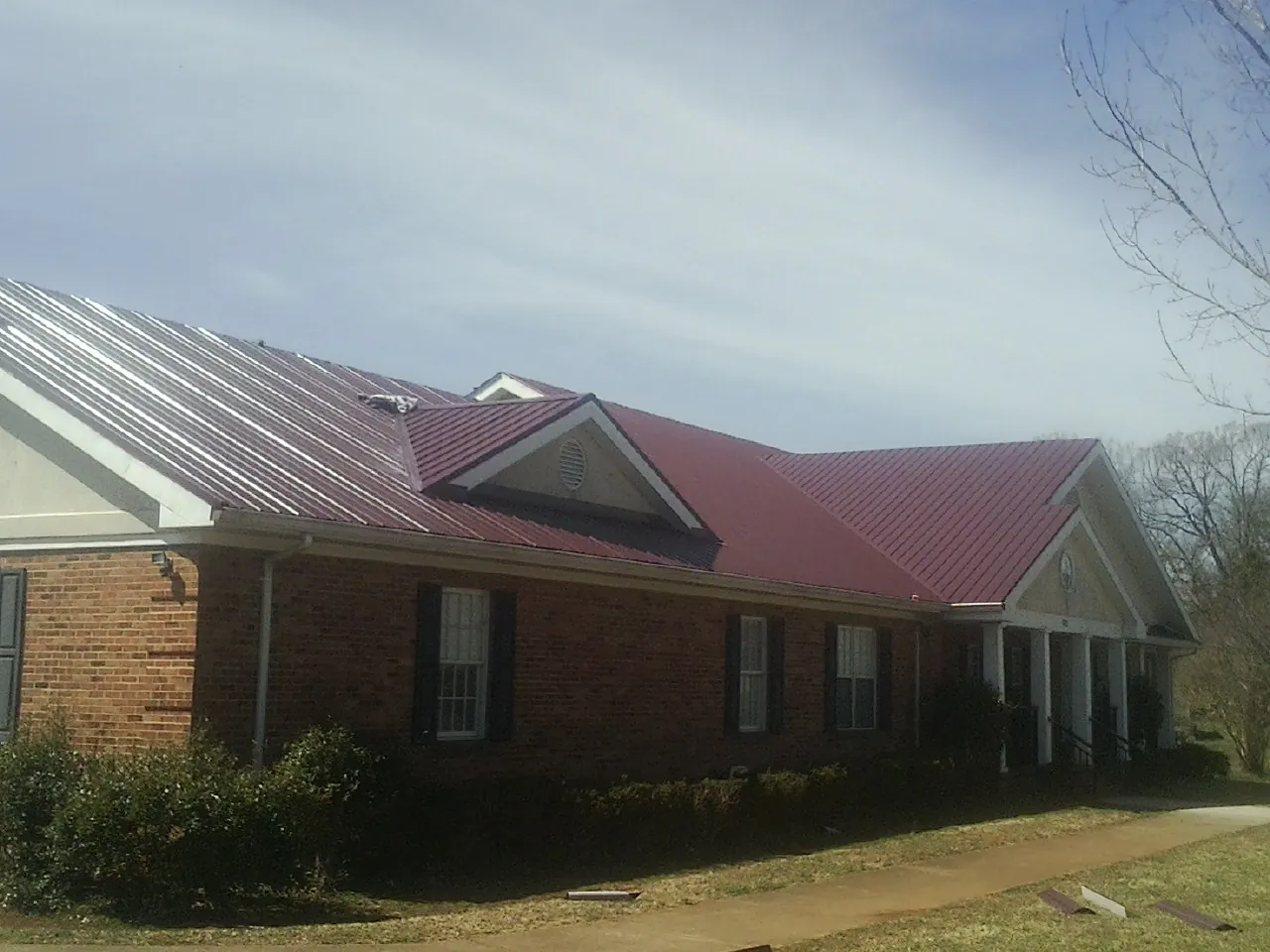 Red metal roof with gabled entries on a long brick building, from a Hail Damage Roof Repair job in North Sandwich