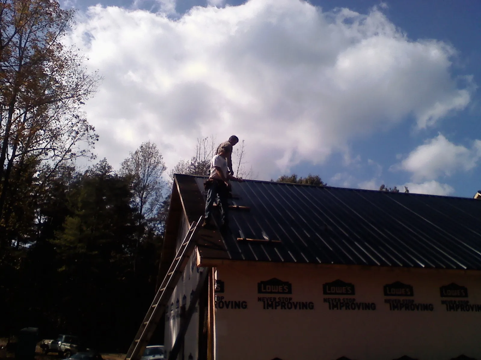 Roofer fastening dark metal panels high against a cloudy sky, from a Roof Inspection job in North Sandwich