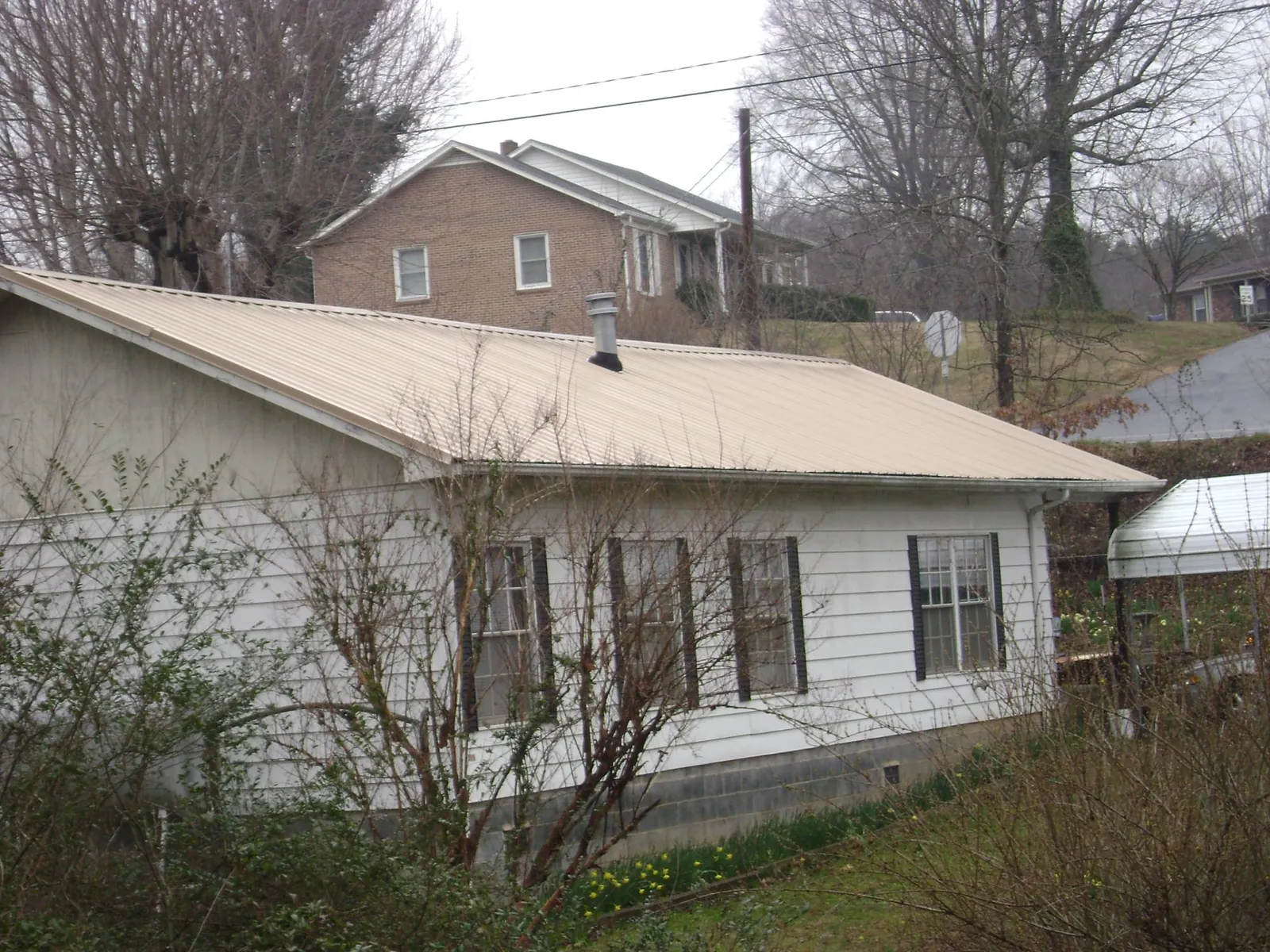 Tan metal roof on a white sided house set into a hillside — Commercial Roofing by Roofing Brothers in North Sandwich